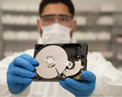 Imagen de cerca de un hombre con guantes y traje de laboratorio, sosteniendo un disco duro expuesto